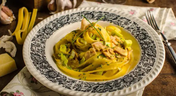 Tagliatelle w kremowym sosie curry z kawałkami kurczaka i porem, udekorowane szczypiorkiem.