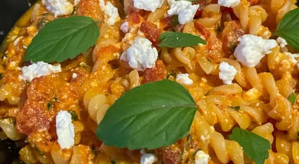 Makaron fusilli z sosem pomidorowym, kawałkami sera feta i listkami bazylii. Pyszne danie, które zachwyci każdego miłośnika pomidorów z fetą.