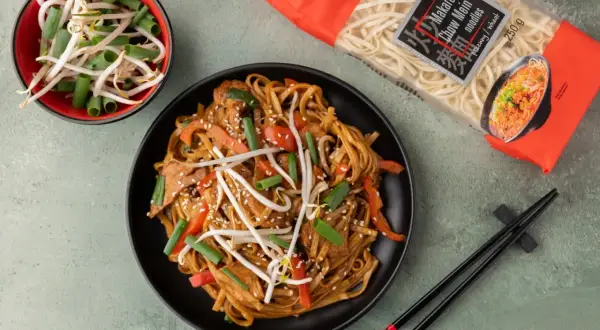 Pyszny makaron chiński z kurczakiem, papryką i kiełkami fasoli mung, gotowy do spożycia. Obok opakowanie makaronu Chow Mein.