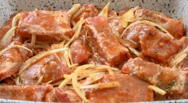 Surowe żeberka pieczone w marynacie z cebulą i przyprawami, gotowe do pieczenia.