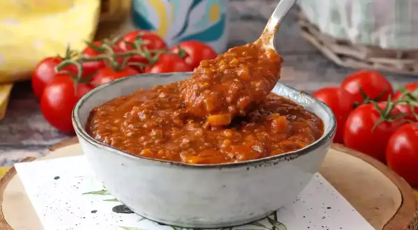 Miseczka sosu bolońskiego z pomidorami w tle.