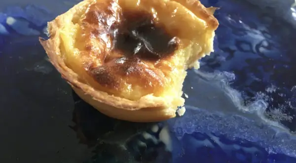 Pyszne, lekko przypalone pastel de nata na niebieskim talerzu. Kruche ciasto i kremowe nadzienie.