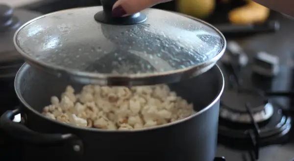 Ręka podnosi pokrywkę garnka, spod której widać gotowy popcorn. Tak właśnie robi się popcorn w garnku!