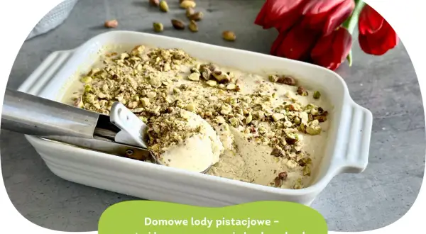 Kremowe lody pistacjowe w białej formie, posypane orzechami. Obok czerwone tulipany.