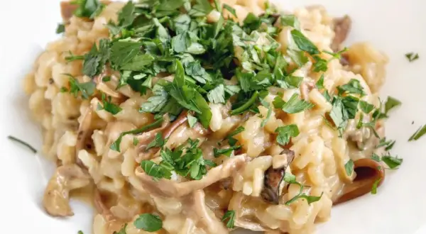 Kremowe risotto z grzybami, posypane świeżą natką pietruszki. Idealne danie dla miłośników leśnych smaków.