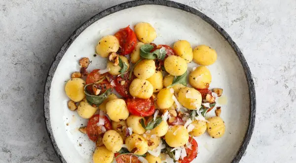 Pyszne gnocchi z pomidorkami koktajlowymi, orzechami i szałwią. Danie posypane parmezanem.