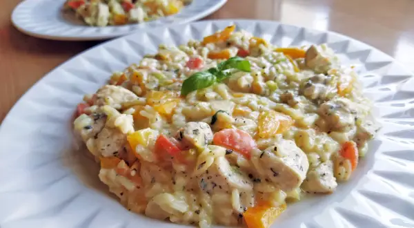 Pyszne risotto z kurczakiem, papryką i ziołami, udekorowane listkiem bazylii. Idealne na obiad.