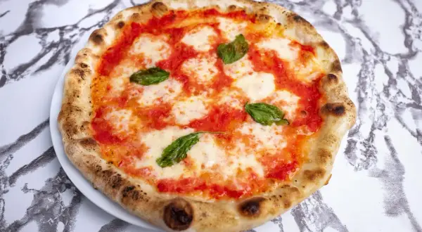 Pyszne ciasto na pizzę neapolitańską, z sosem pomidorowym, mozzarellą i listkami bazylii, na marmurowym tle.
