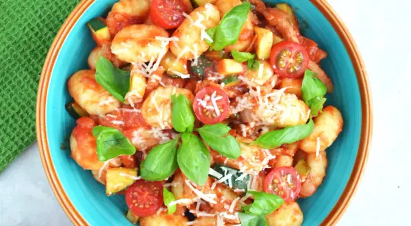 Pyszne gnocchi z sosem pomidorowym, cukinią, pomidorkami koktajlowymi i bazylią, posypane parmezanem.