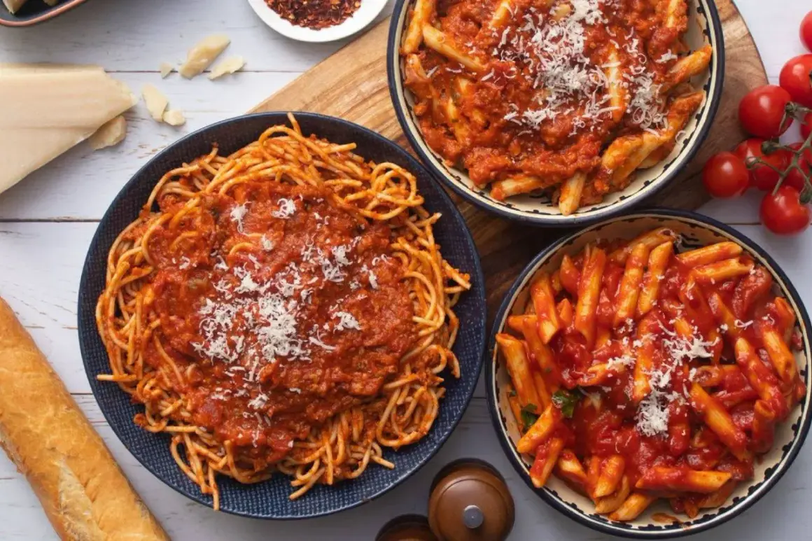 Pyszny obiad bez mięsa: spaghetti i penne w sosie pomidorowym, posypane parmezanem. Obok bagietka i pomidorki.