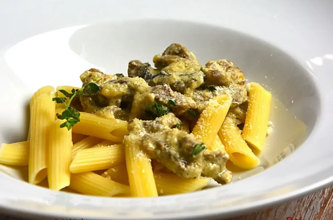 Penne z kremowym sosem i kawałkami wołowiny, posypane parmezanem i udekorowane gałązką ziół. Pyszny makaron z wołowiną.