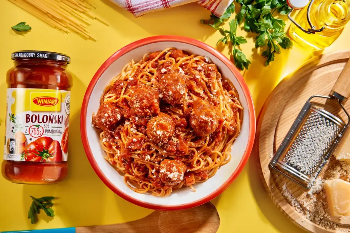 Pyszne spaghetti bolognese z klopsikami w sosie pomidorowym, obok słoik sosu i tarka z parmezanem.