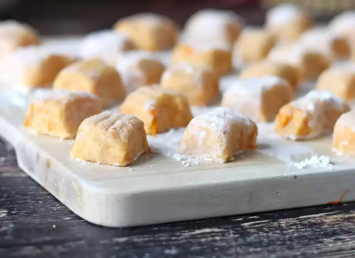 Pomarańczowe gnocchi z dyni, posypane cukrem pudrem, ułożone na desce.