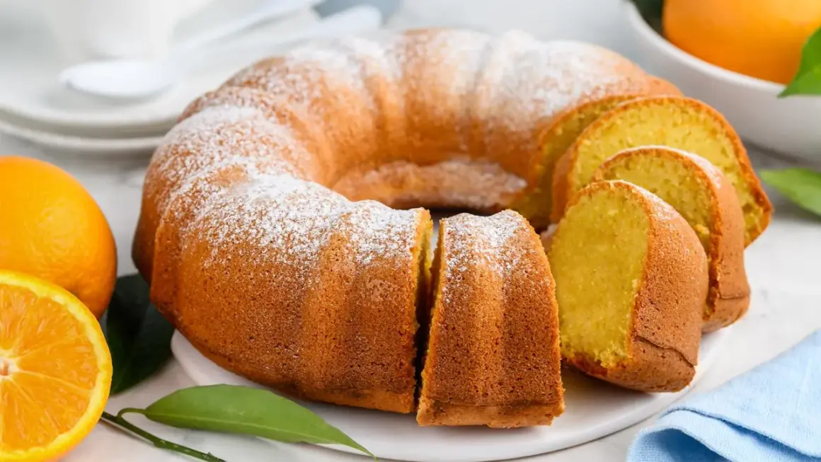 Puszysta babka piaskowa, oprószona cukrem pudrem, z pomarańczami w tle. Idealna na deser.