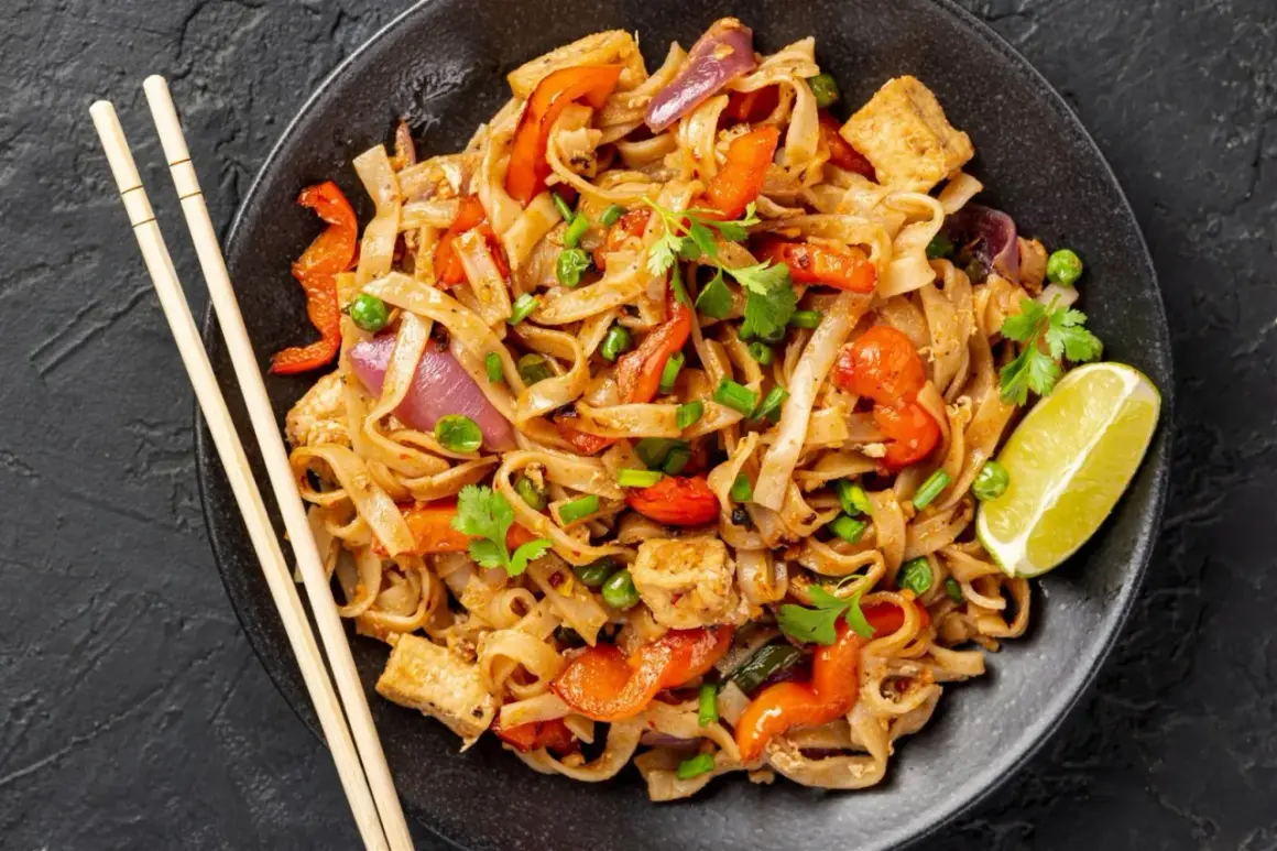 Pyszny pad thai z kurczakiem, warzywami i makaronem ryżowym, udekorowany kolendrą i ćwiartką limonki.