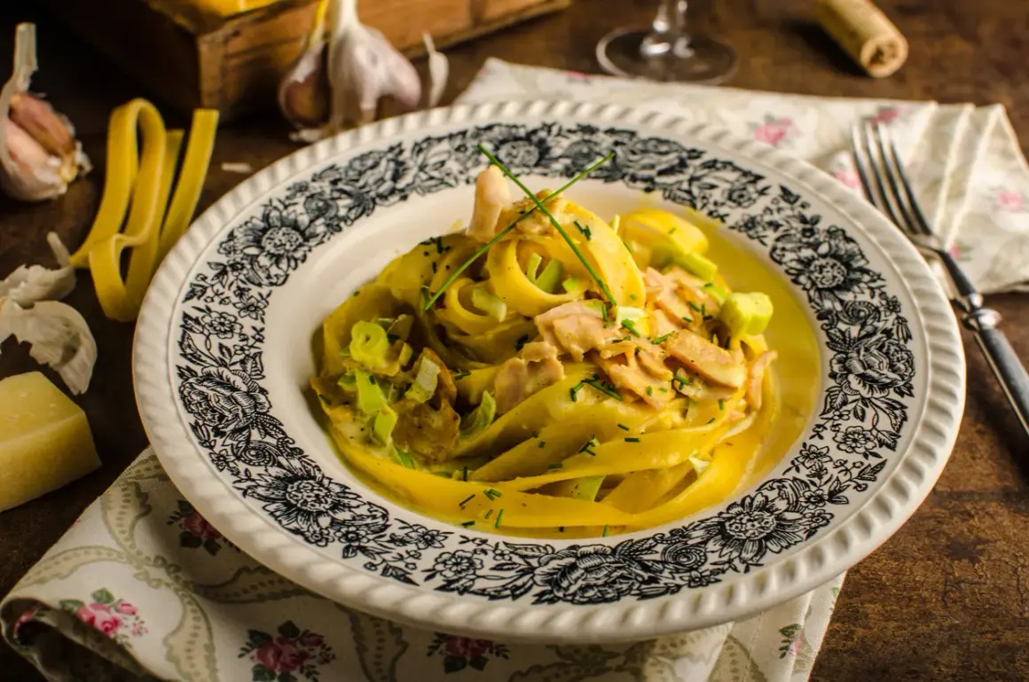 Tagliatelle w kremowym sosie curry z kawałkami kurczaka i porem, udekorowane szczypiorkiem.
