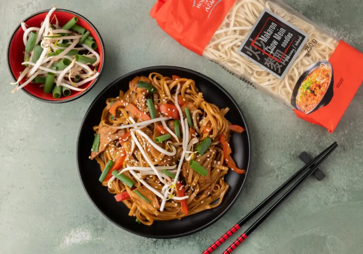 Pyszny makaron chiński z kurczakiem, papryką i kiełkami fasoli mung, gotowy do spożycia. Obok opakowanie makaronu Chow Mein.