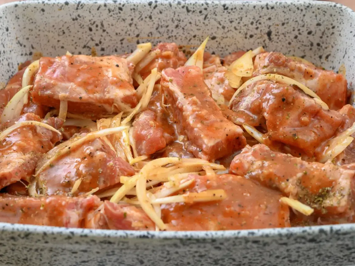 Surowe żeberka pieczone w marynacie z cebulą i przyprawami, gotowe do pieczenia.