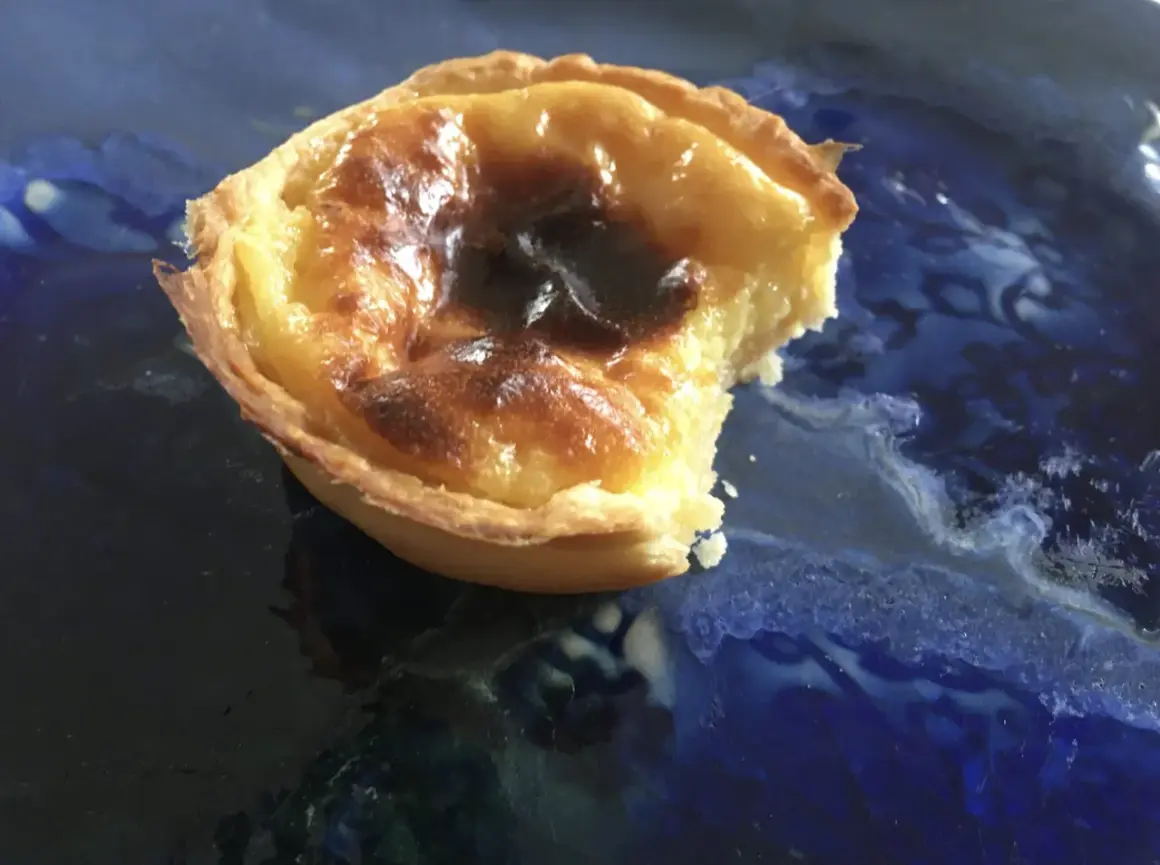 Pyszne, lekko przypalone pastel de nata na niebieskim talerzu. Kruche ciasto i kremowe nadzienie.