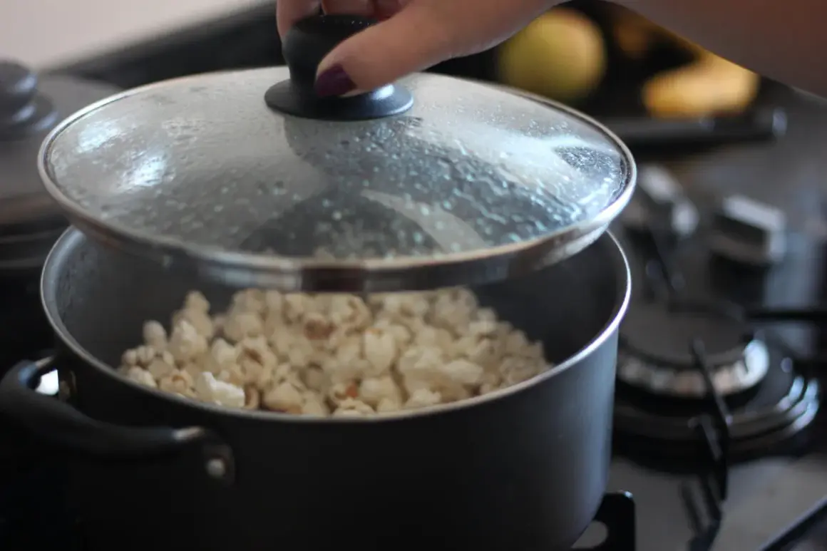 Ręka podnosi pokrywkę garnka, spod której widać gotowy popcorn. Tak właśnie robi się popcorn w garnku!