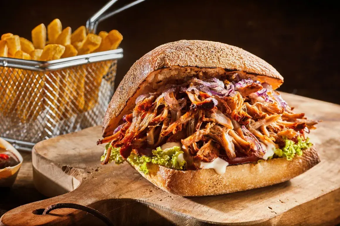 Soczysty pulled pork w bułce, z czerwoną cebulą i sałatą, obok frytki. Idealny pulled pork przepis na obiad.