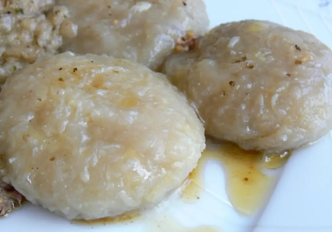 Trzy okrągłe, lekko błyszczące szare kluski polane sosem na białym talerzu.