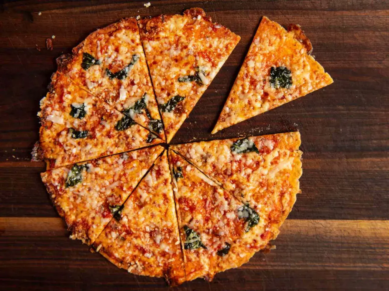 Chrupiąca pizza z tortilli, pokrojona na kawałki, z serem i bazylią, na drewnianej desce.