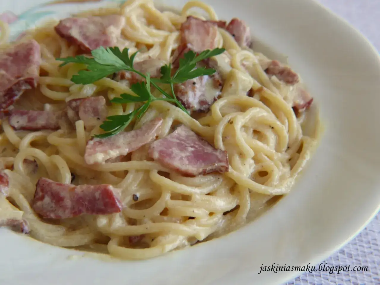 Pyszne spaghetti carbonara z chrupiącym boczkiem i kremowym sosem, udekorowane natką pietruszki.