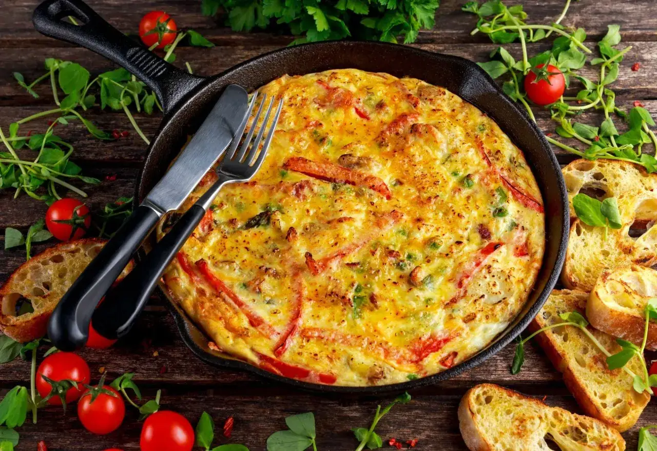 Złocista frittata z ziemniakami, papryką i ziołami w żeliwnej patelni, podana z chrupiącym pieczywem i pomidorkami.