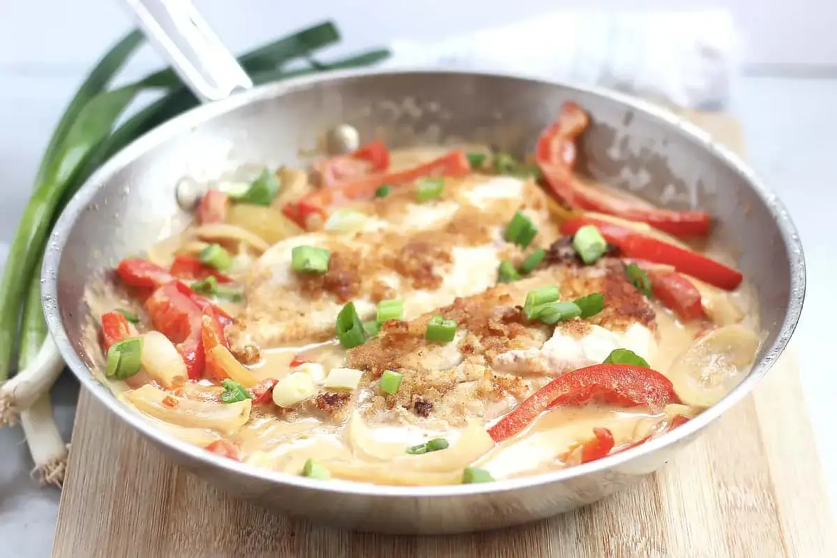 Pyszny makaron w sosie curry z kawałkami kurczaka, papryką i szczypiorkiem, podany na patelni.