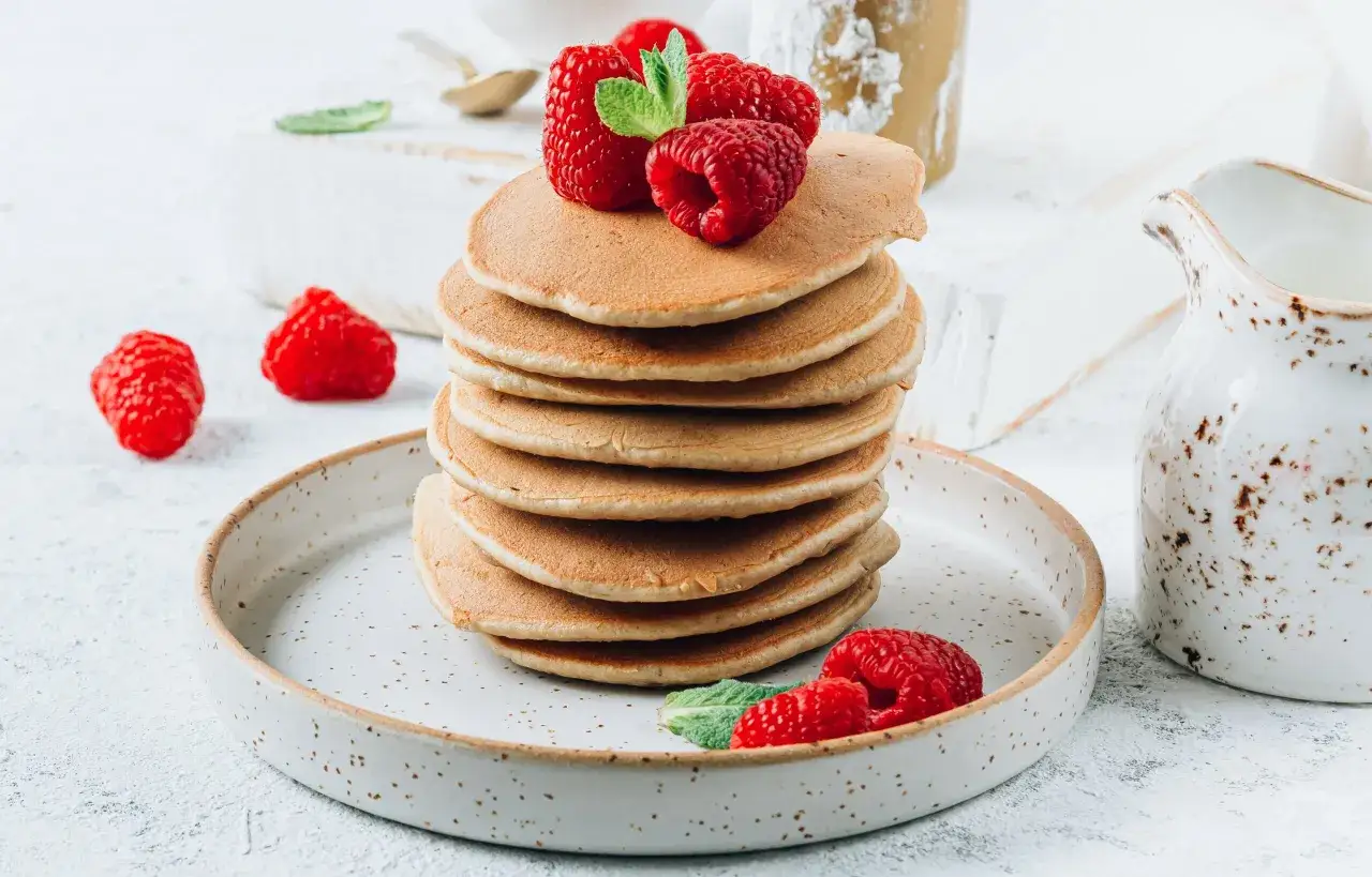 Stos fit pancakes z odżywki białkowej bez banana, udekorowane malinami i miętą, na talerzu.