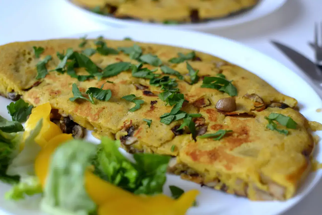 Pyszny omlet z ciecierzycy z pieczarkami, posypany świeżą natką pietruszki, podany z sałatką i papryką.