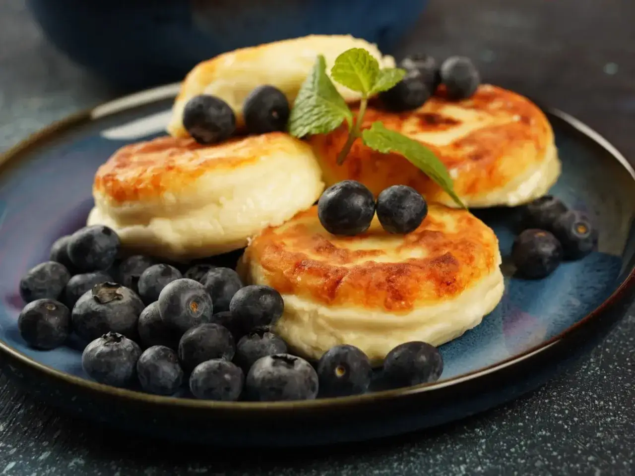 Pyszne pancakes z borówkami, udekorowane listkiem mięty, kuszą apetycznym wyglądem.