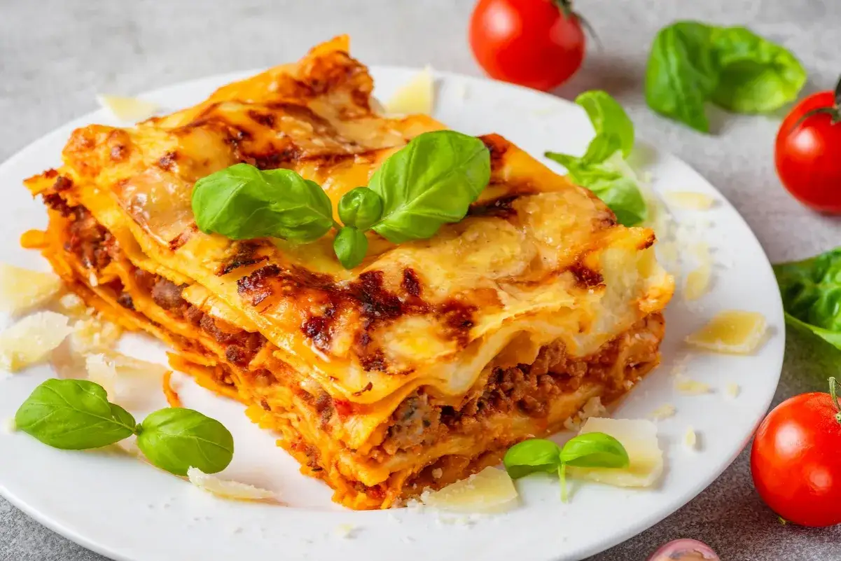Pyszna lasagne z mięsem mielonym i serem, ozdobiona bazylią i pomidorkami. Czy makaron do lasagne trzeba gotować? Nie, jeśli użyjesz świeżego!