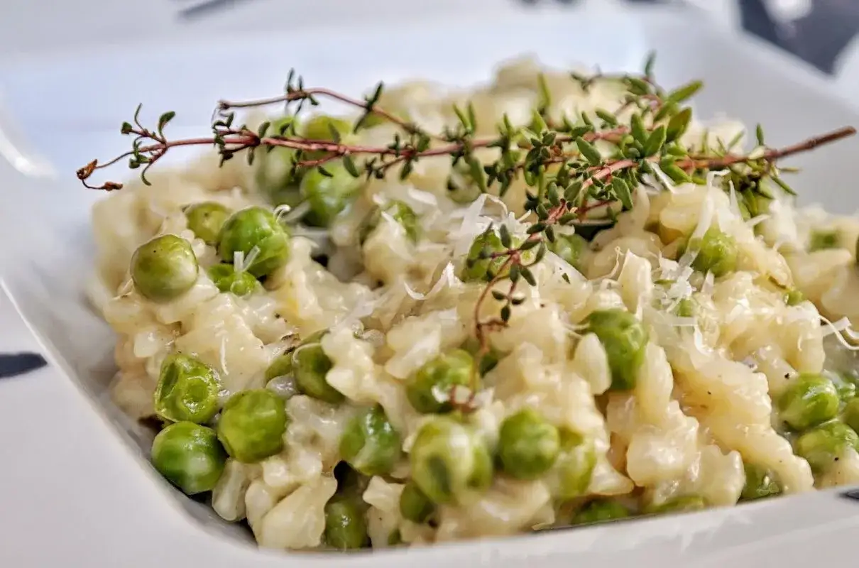 Kremowe risotto z groszkiem, posypane parmezanem i udekorowane gałązką tymianku. Pyszne danie, kt&oacute;re zachwyca smakiem.