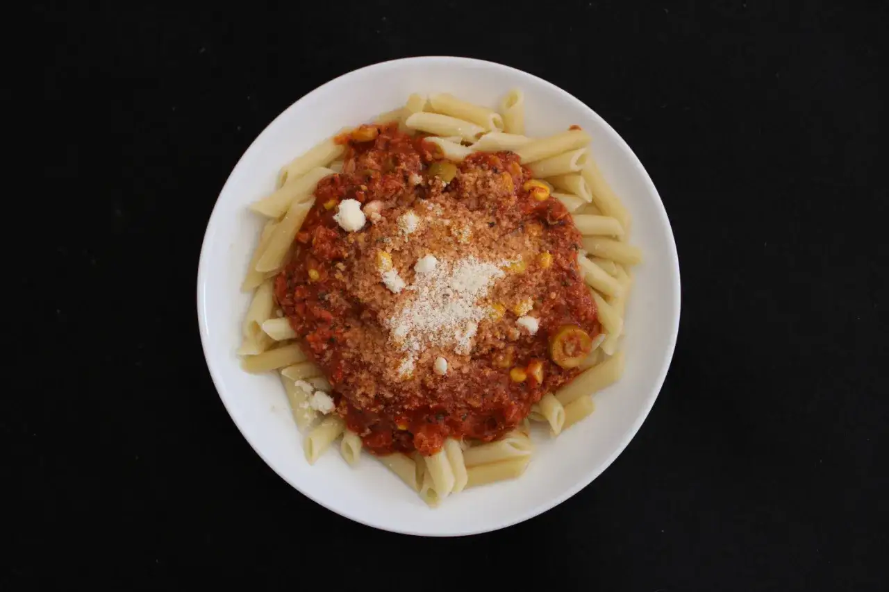 Penne z sosem pomidorowym, tuńczykiem, kukurydzą i oliwkami, posypane parmezanem. Pyszny makaron z tuńczykiem na talerzu.