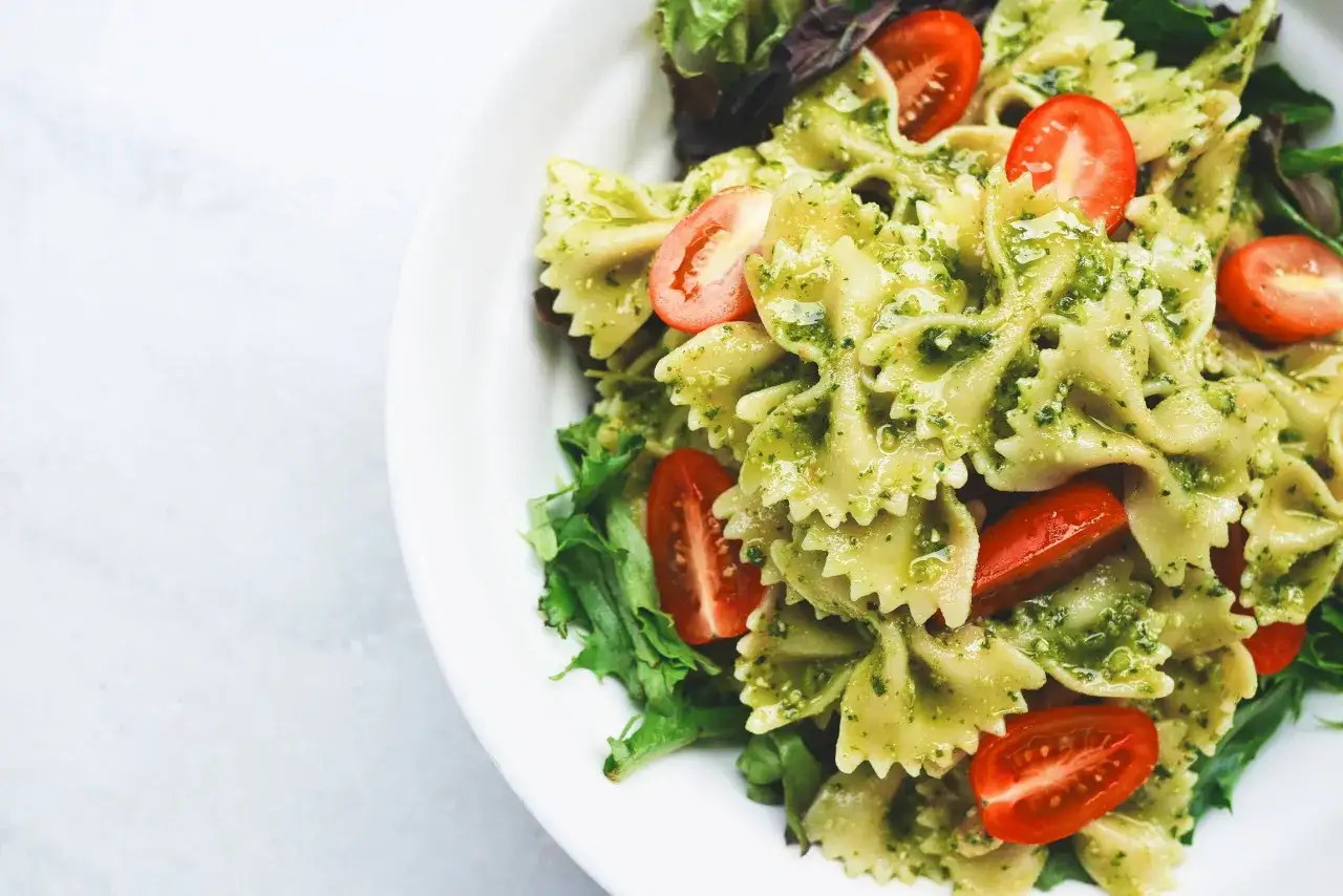 Pyszny makaron z warzywami w sosie pesto, ozdobiony pomidorkami koktajlowymi i świeżą sałatą.