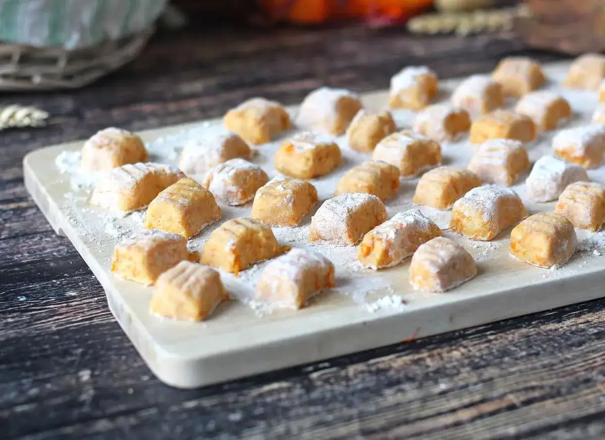 Rządki pomarańczowych gnocchi z dyni, posypane mąką, ułożone na desce.