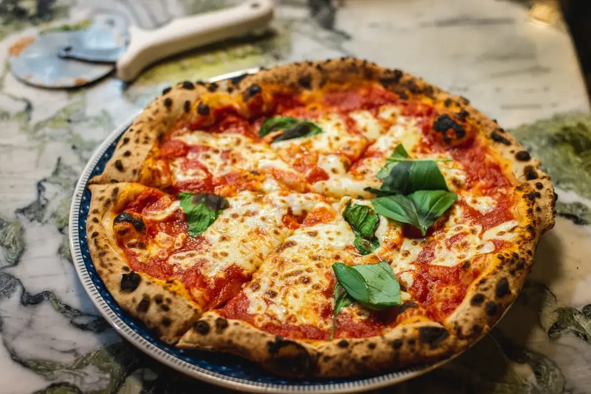 Pyszne ciasto na pizzę neapolitańską z pomidorami, mozzarellą i bazylią, gotowe do pokrojenia.