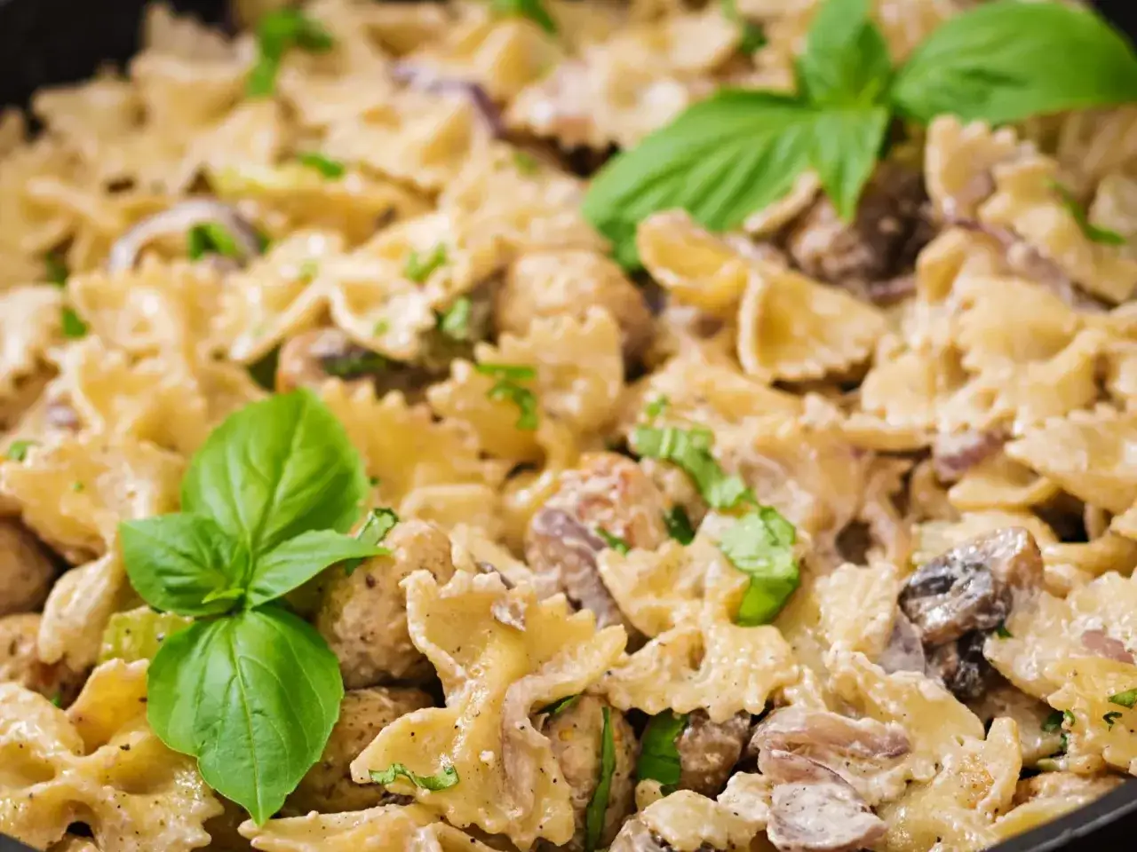 Pyszne, nowoczesne dania jednogarnkowe: makaron farfalle w kremowym sosie z kurczakiem, pieczarkami i bazylią.