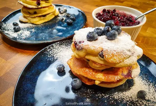 Pyszne pancakes z borówkami, posypane cukrem pudrem i świeżymi owocami. Idealne na śniadanie.