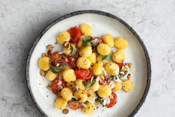 Pyszne gnocchi z pomidorkami koktajlowymi, orzechami i szałwią. Danie posypane parmezanem.