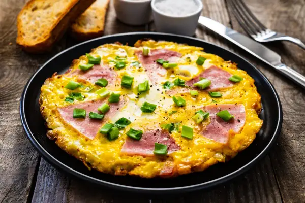 Pyszny omlet z szynką i serem, posypany szczypiorkiem. Idealny pomysł na śniadanie, jak zrobić omlet z szynką i serem.