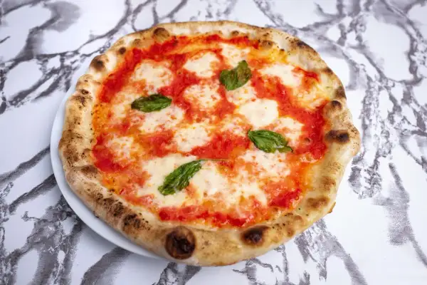 Pyszne ciasto na pizzę neapolitańską, z sosem pomidorowym, mozzarellą i listkami bazylii, na marmurowym tle.